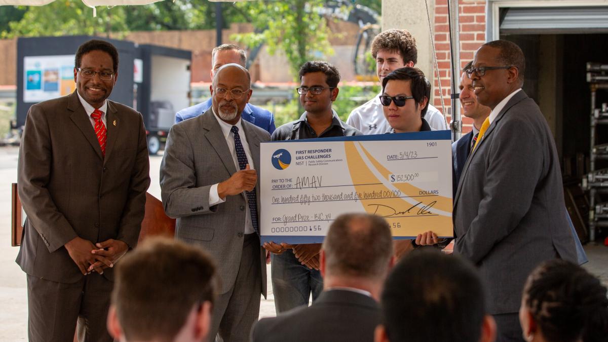 Congressman Glenn Ivey is joined by UMD President Darryll Pines (on left) and Dean of Engineering School, Samuel Graham, Jr (holding check on right) presenting check to two of the four team members, Animesh Shastry (L) and Qingwen Wei (R).