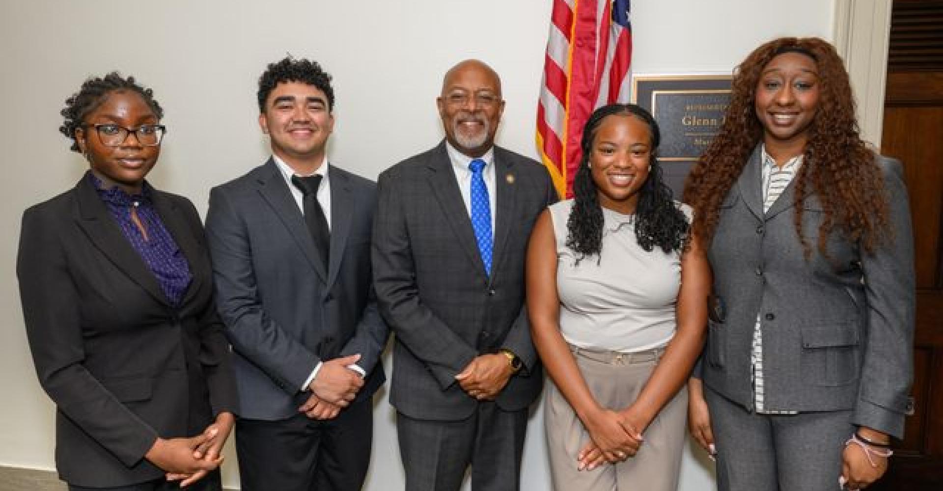 A man with classes smiling for a photo with 3 young adults 