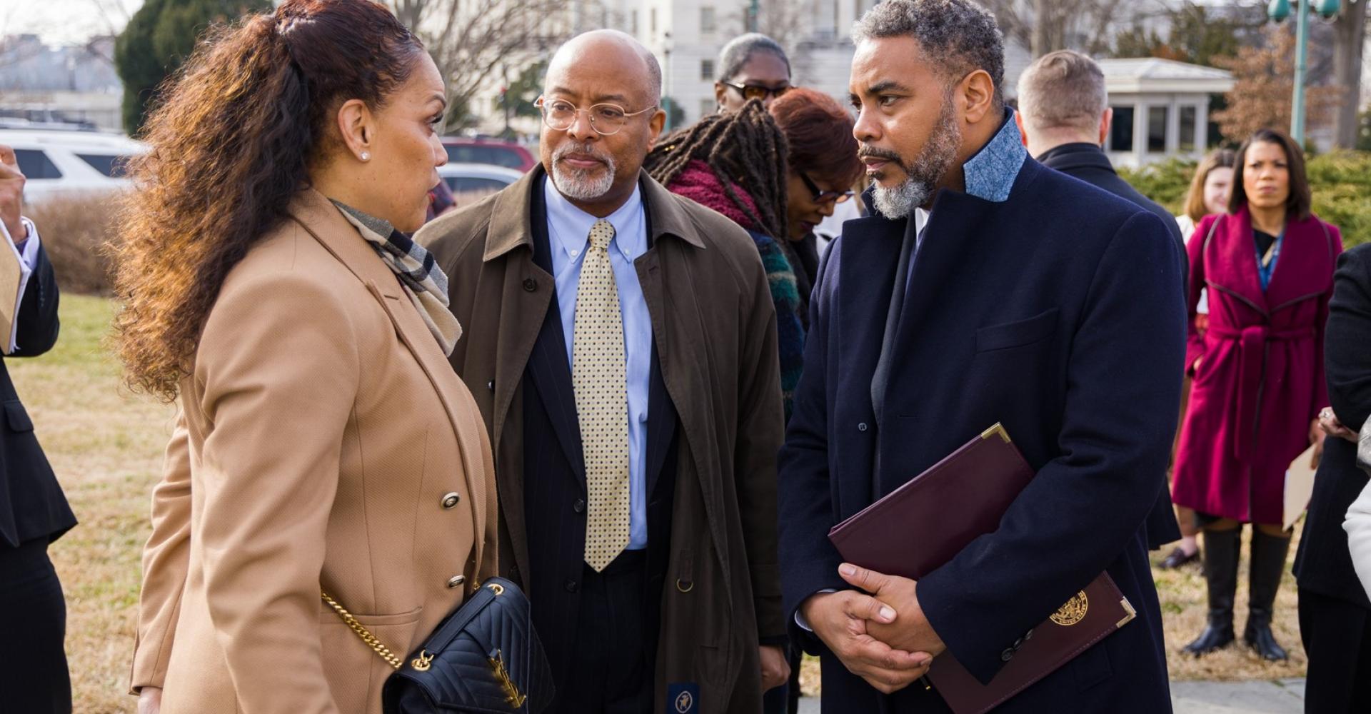 Two men in suits standing next to a woman. 