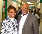 Man and woman standing next to each other smiling for a photo in the hallway of a school. 